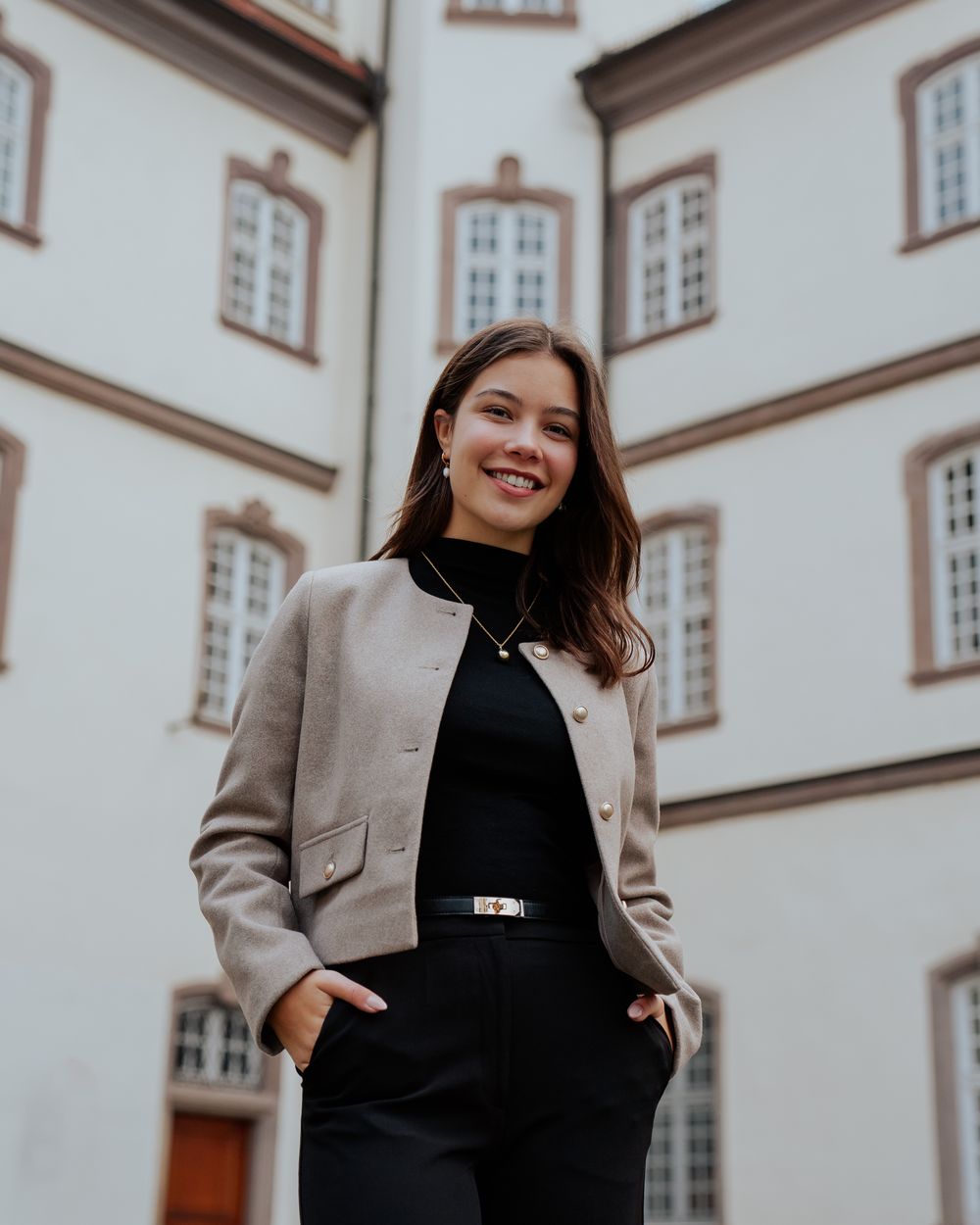 Frau im hellen Blazer vor einem weißen Schlossgebäude
