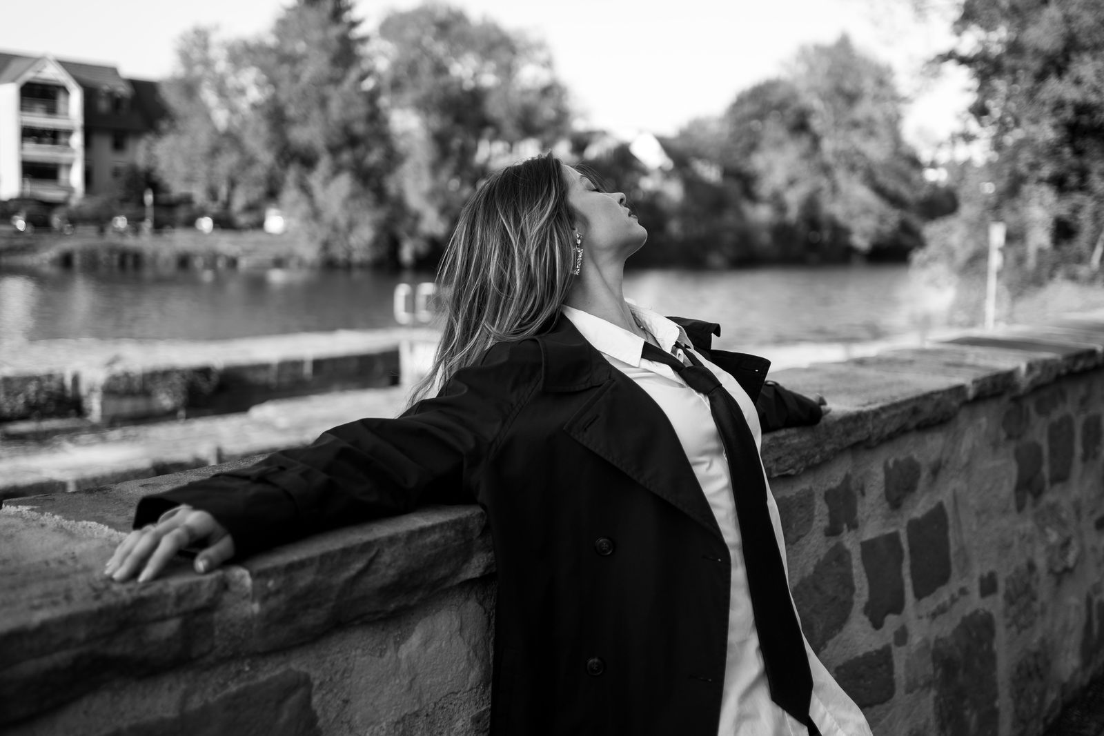 Schwarzweiß: Frau lehnt sich mit geschlossenen Augen an eine Mauer am Wasser
