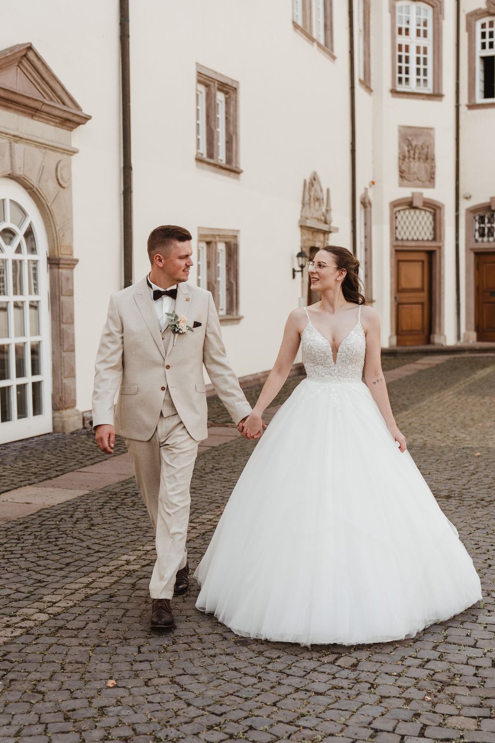 Brautpaar läuft Hand in Hand über den Schlosshof
